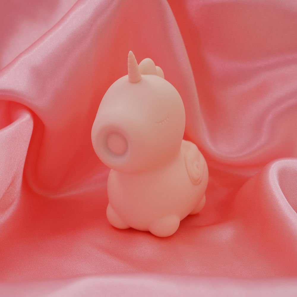 Side view of the Unihorn Heart Throb pulsing clitoral stimulator, close-up on the pulsating tip, placed on pink satin fabric | Flirty Bay adult store and lingerie store